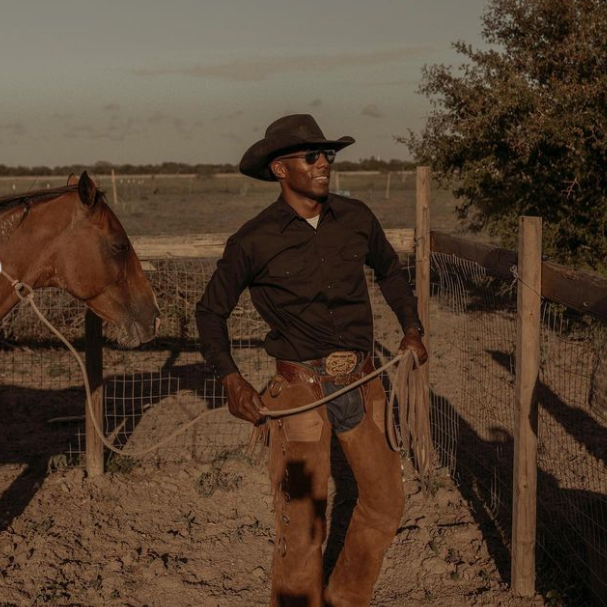 Cowboy wearing a hat and a belt buckle with a horse on a plain 